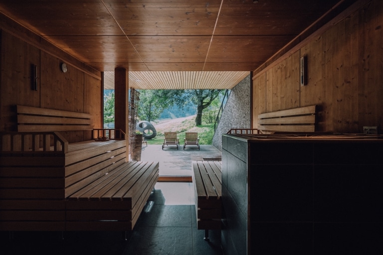 Blick durch die Sauna auf Holzterrasse mit Liegen des AlpinSpa