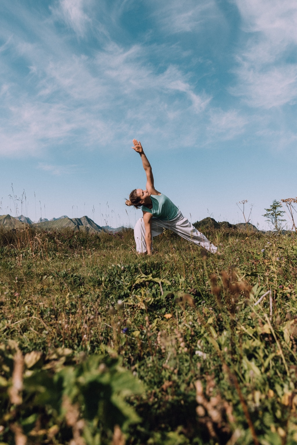 Frau beim Yoga in den Bergen auf grüner Wiese