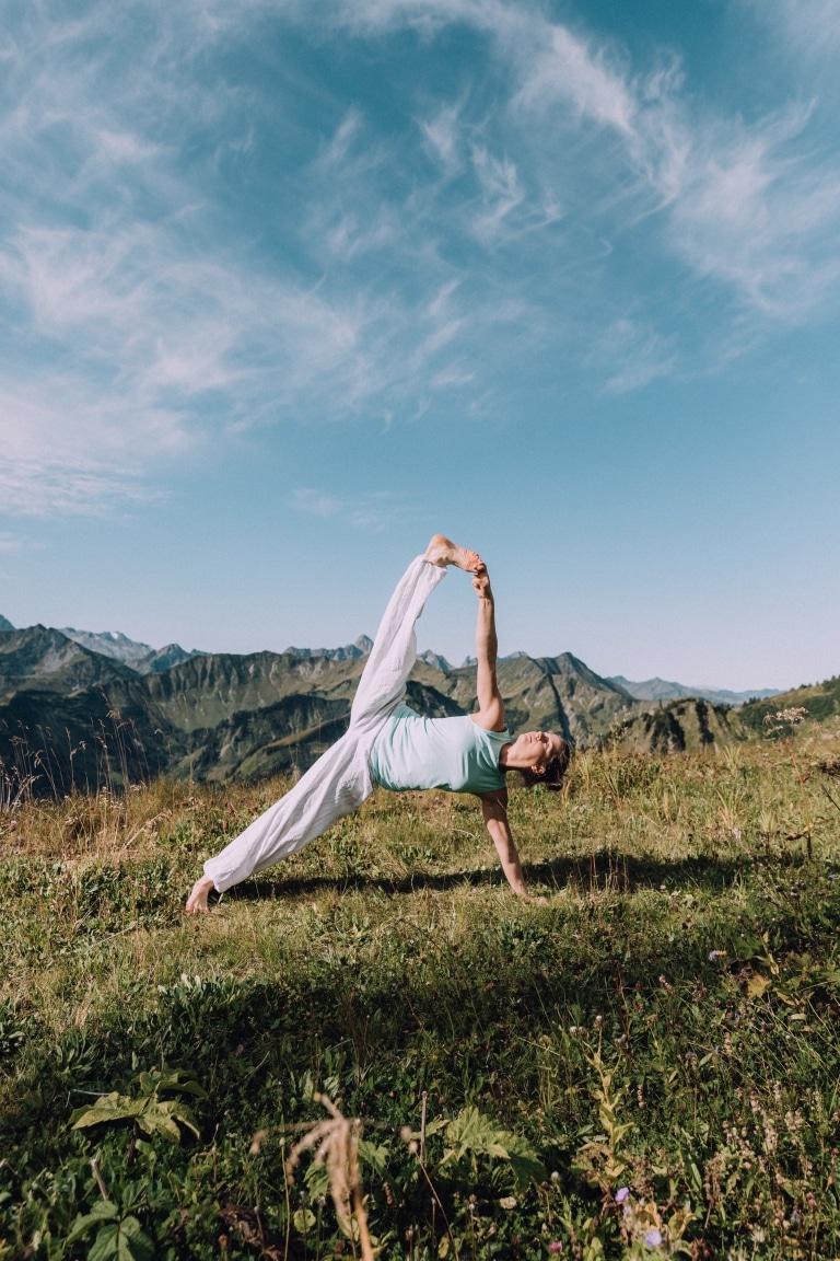 Frau macht Yoga in den Bergen unter blauem Himmel