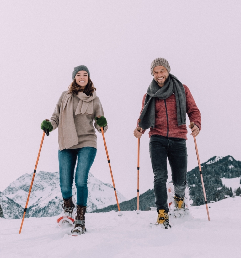 Magdalena und Manuel laufen beim Schneeschuhwandern auf die Kamera zu