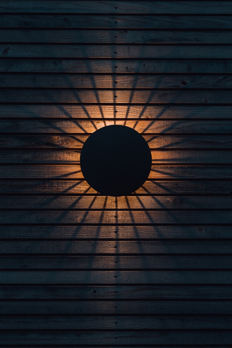 Lampe wirft sonnenförmigen Schatten auf Holzfassade am Chalet