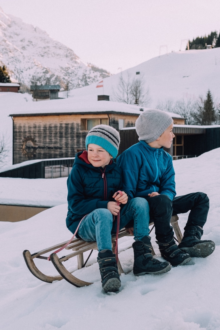 Kinder sitzen auf Schlitten im Schnee hinterm Chesa Valisa