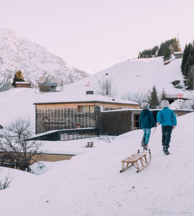 Kinder ziehen Schlitten hinter dem Naturhotel