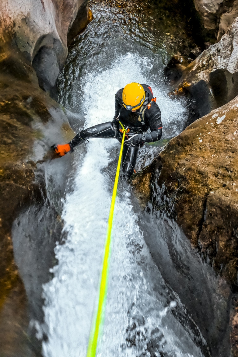 Canyoning Mann klettert einen Wasserfall hoch an Seil gesichert