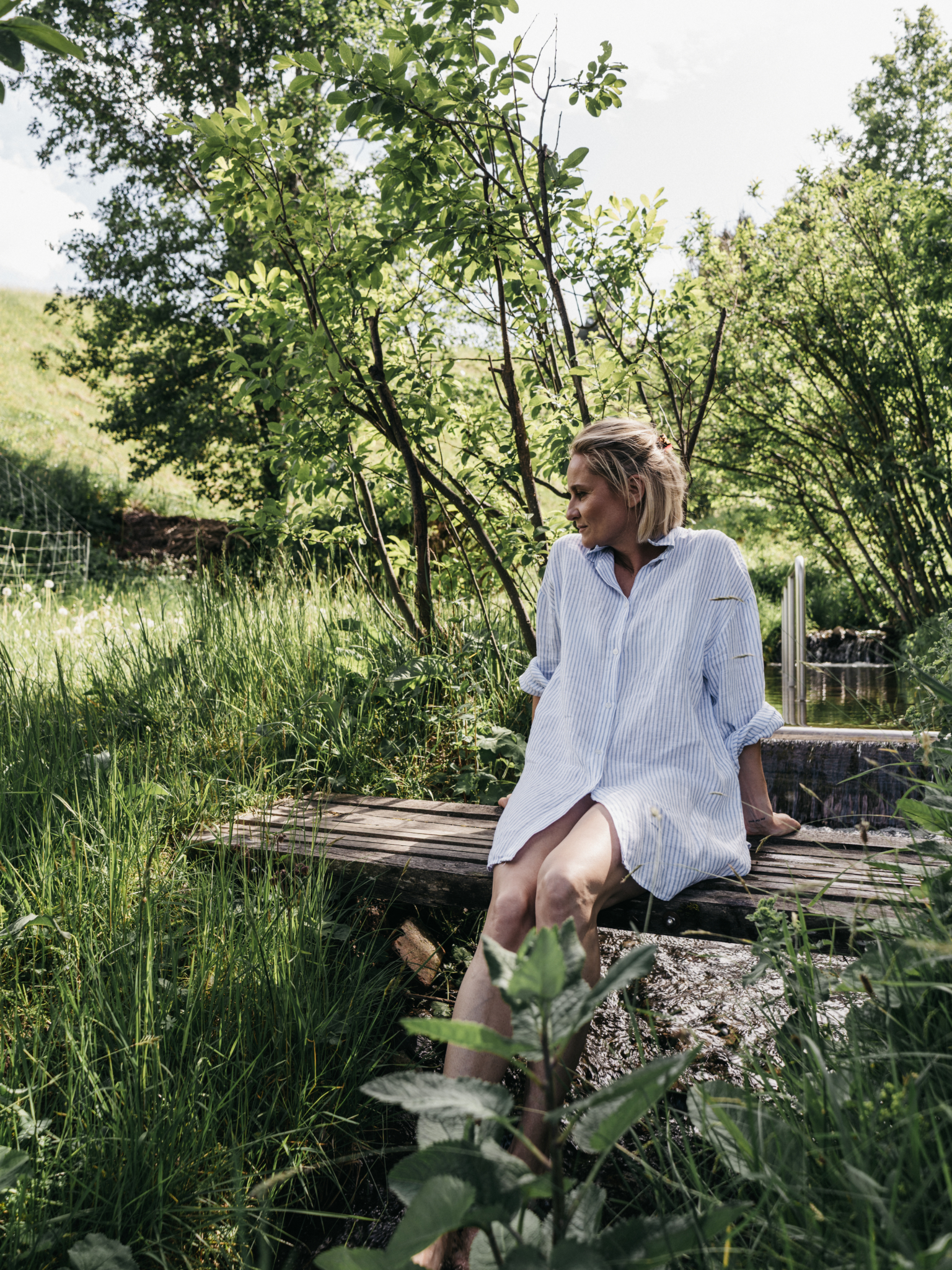 Frau sitzend beim Bach im Garten